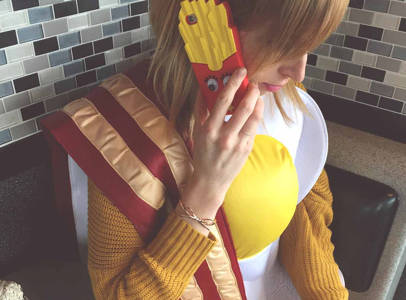 Girl in egg costume talking on mobile phone with french fry case