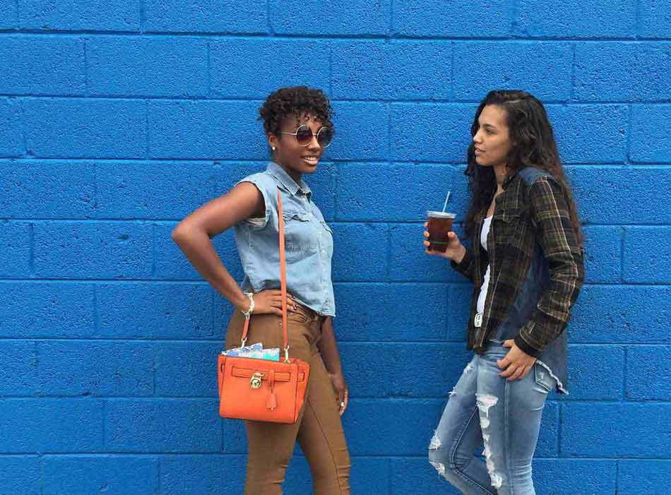 Two girls leaning on blue wall talking